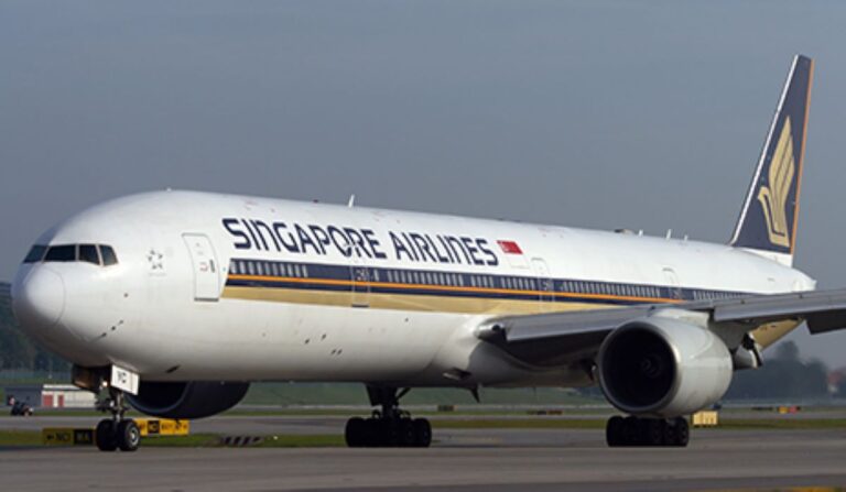 Singapore Airlines widebody aircraft parked on the taxiway, fuselage text reads SINGAPORE AIRLINES with yellow-black stripe along the side, engine visible under wing, tail logo visible