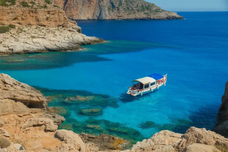 Small white boat with a blue canopy anchored in crystal-clear turquoise water near rocky cliffs.