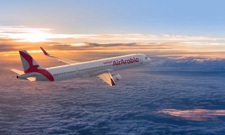 Air Arabia passenger jet flying above clouds at sunset.