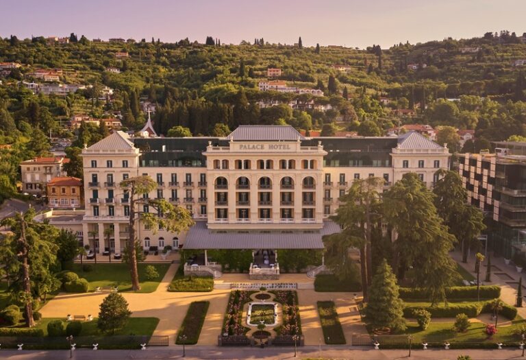 Aerial view of the Palace Hotel—a large white neoclassical building with a formal entrance, surrounded by manicured gardens and a central fountain.