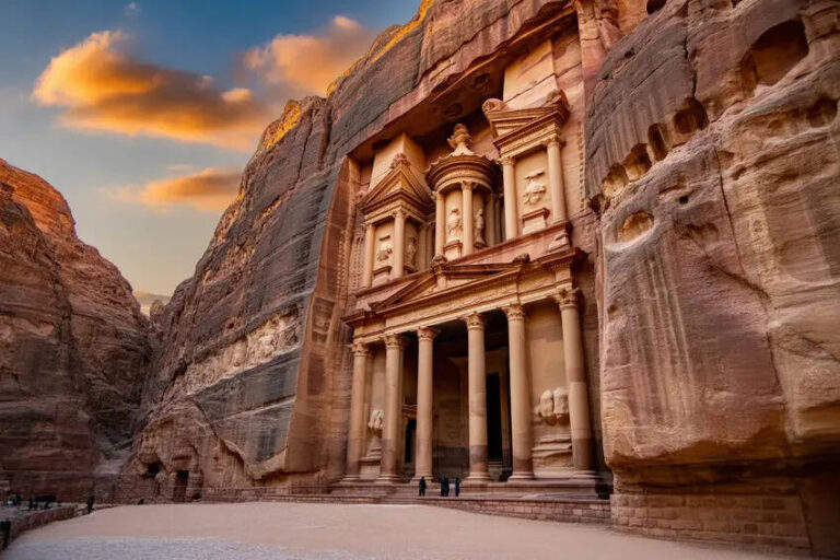Rock-cut facade of the Treasury at Petra, Jordan, with columns carved into a sandstone cliff at sunset, showing visitors for scale.