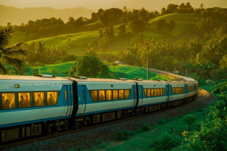 Modern white passenger train rounding a green hillside, bathed in warm golden light at sunset.