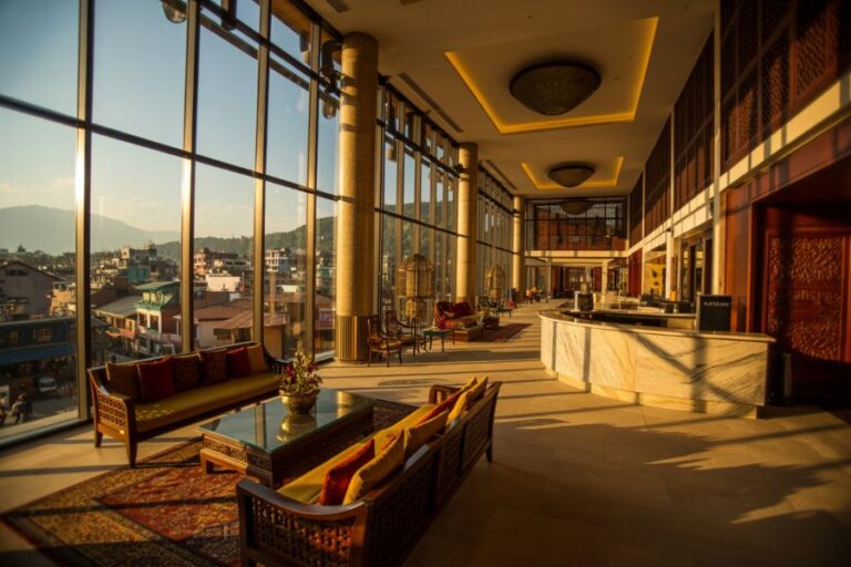 Luxurious hotel lobby with floor-to-ceiling windows, plush seating, and a marble reception desk bathed in warm sunset light.