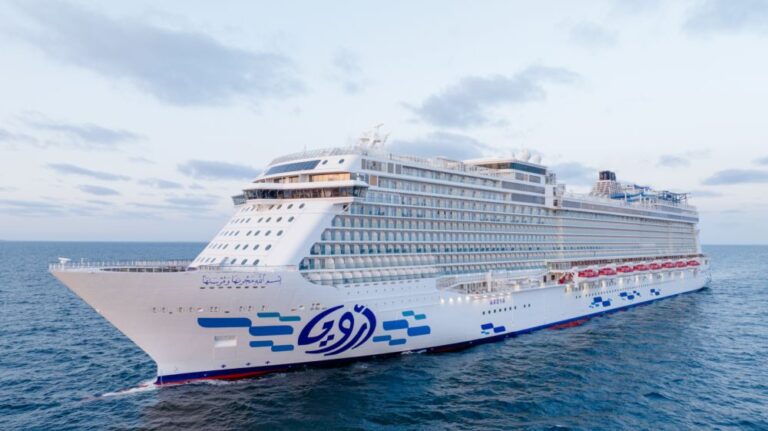 White cruise ship with many decks sailing on calm ocean under a cloudy sky.