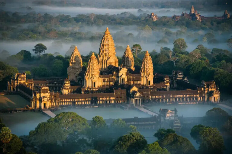 Angkor Wat temple complex surrounded by misty jungle at dawn, with tall central towers and surrounding moats and walls in warm light across the scene.