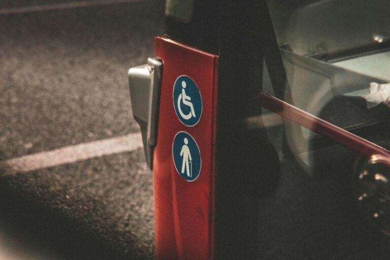 Red bus door post displaying blue accessibility icons for wheelchair users and a standing person/pedestrian to indicate accessibility features.