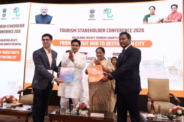 Four people on a stage exchange folders during the Tourism Stakeholder Conference 2026, with a banner behind them promoting transit hubs to destination city ideas.