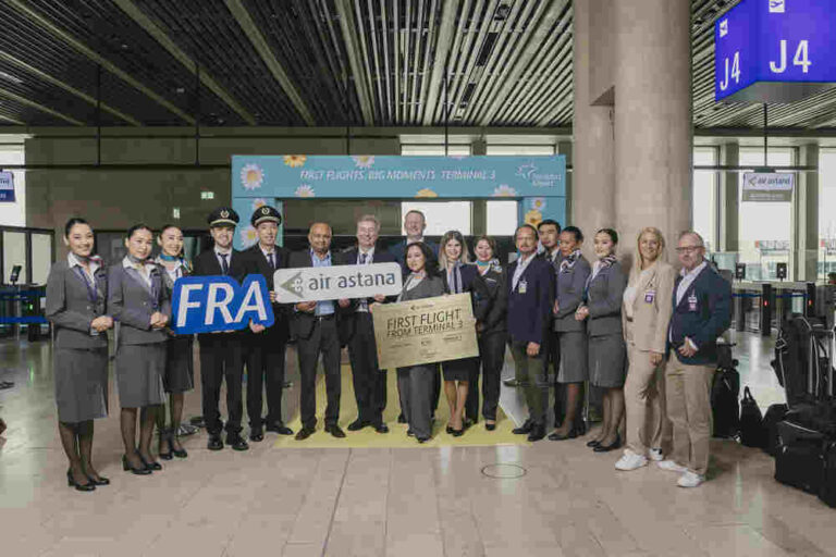 Group of airline staff and pilots posing at an airport terminal with signs for FRA and Air Astana First Flight from Terminal 1/2.
