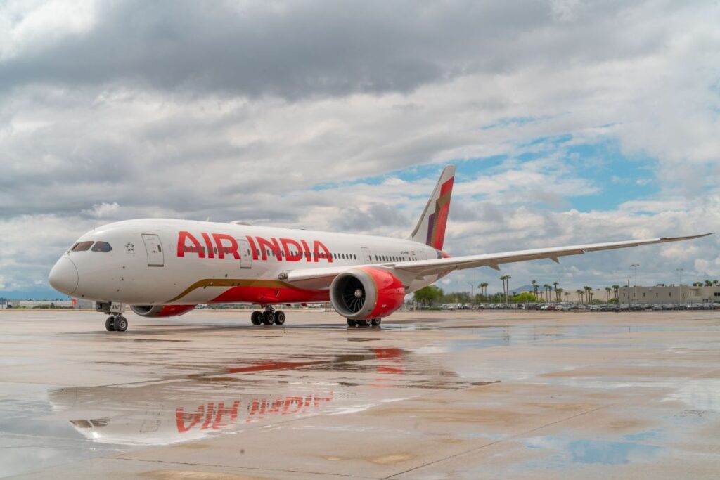 Air India passenger jet on a wet tarmac with a cloudy sky overhead and its reflection in a puddle