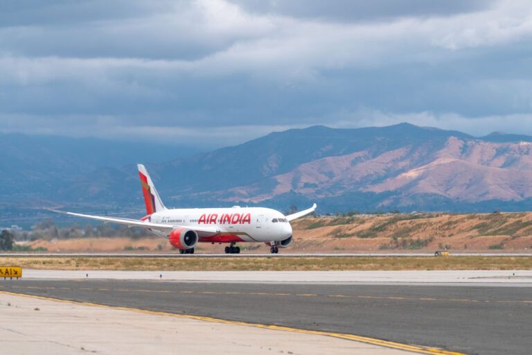 Air India passenger aircraft on a runway with mountains under a cloudy sky in the background.