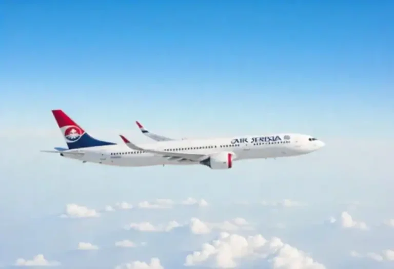 Air Serbia passenger jet flying above white clouds under a clear blue sky, logo visible on the tail fin.