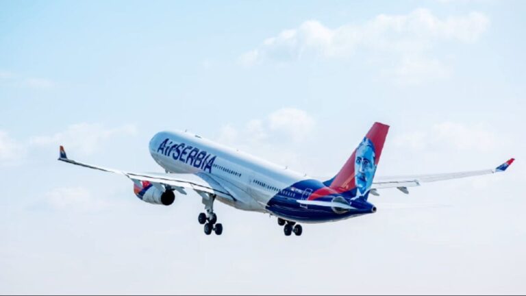 Airline jet with blue-and-white livery and a portrait on the tail lifting off against a blue sky.