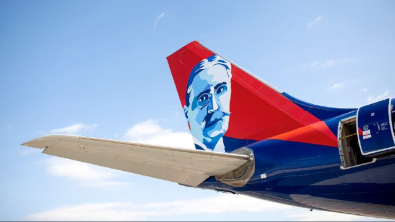 Airplane tail with a red and blue mural of a mustached man against a clear blue sky