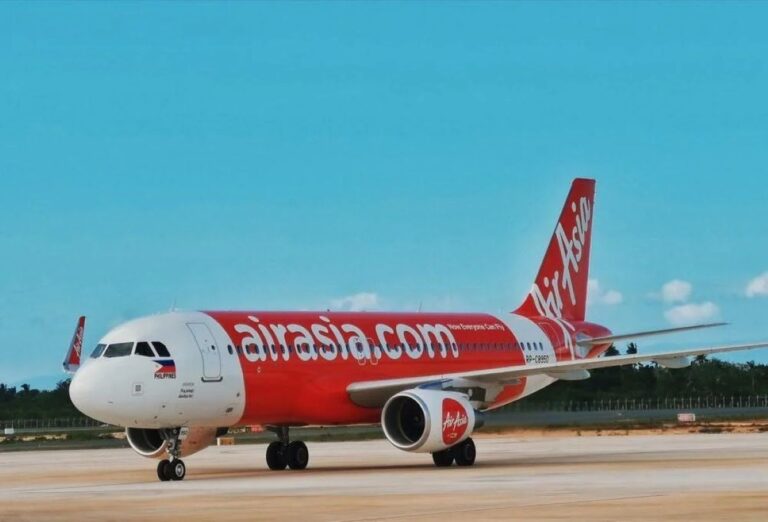 AirAsia jet on the runway with red-and-white livery and 'airasia.com' painted along the fuselage.