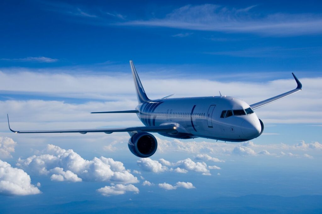 Commercial passenger jet flying above the clouds in a blue sky.