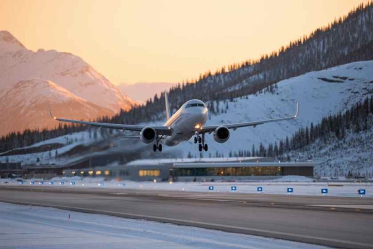 Airplane landing on a snow-covered runway with snow-dusted mountains at sunset.