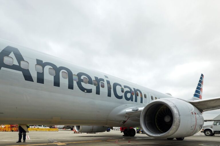 Close-up of an American Airlines jet on the tarmac, showing the engine and the bold 'American' branding on the fuselage.