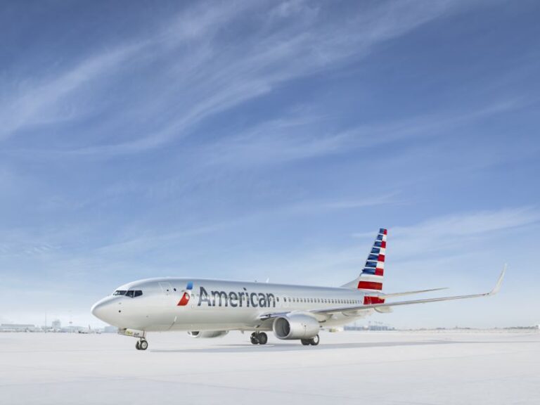 American Airlines passenger jet on a snow-covered tarmac under a clear blue sky, ready for taxi or takeoff.