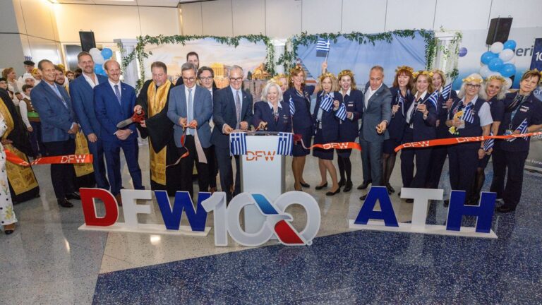 Group of officials and staff at a ribbon-cutting ceremony for DFW100ATH, holding Greek flags with balloons in the background.