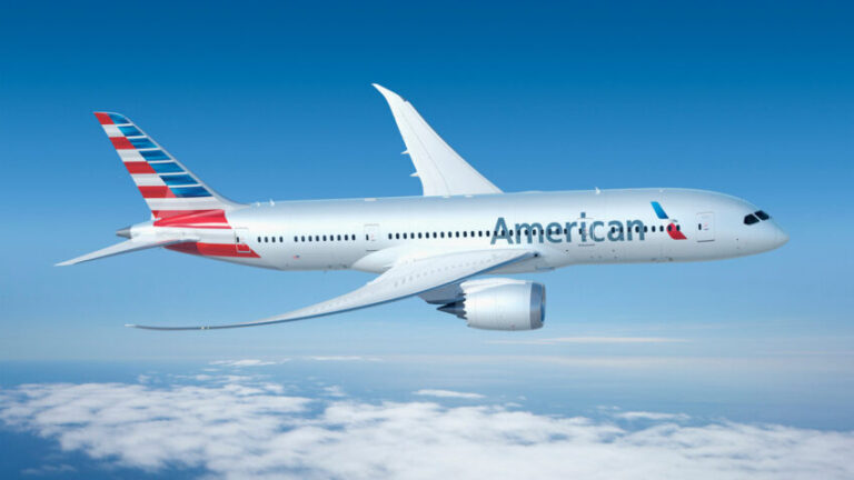 American Airlines plane in flight above wispy clouds with a clear blue sky, engines visible beneath the wings.
