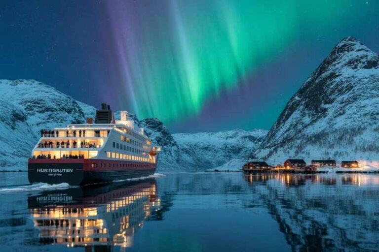Cruise ship named Hurtigruten gliding through a icy fjord under the Northern Lights with snow-covered mountains on both sides.