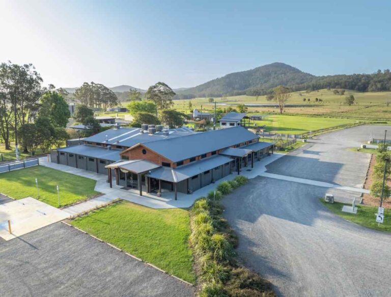 A modern low-rise building with a metal roof on a rural campus, surrounded by green fields and distant hills.