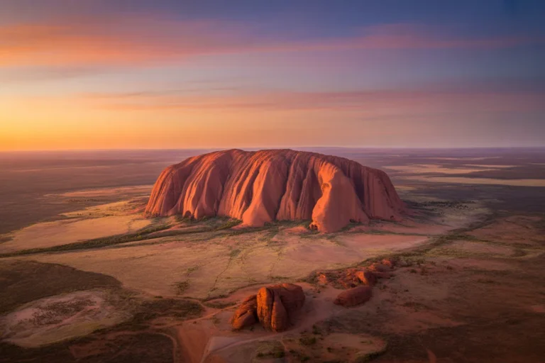 Sunset over Uluru, the large red rock formation glowing orange in a flat desert landscape