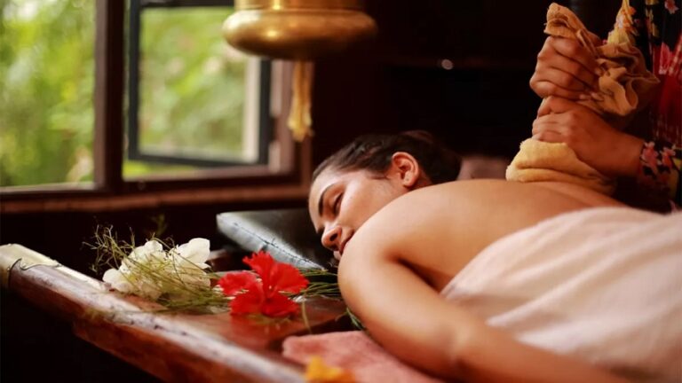 Person receiving a back massage on a massage table with a therapist pressing along the spine, flowers on the table nearby.