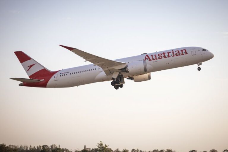 Austrian Airlines passenger jet lifting off from the runway at sunset with landing gear extended.