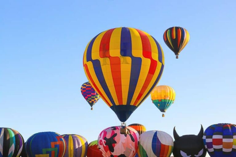 Colorful hot air balloons rise into a clear blue sky, with a row of decorated balloons in the foreground.