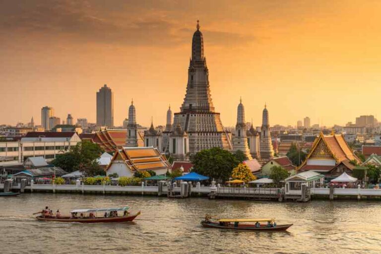 Sunset over Bangkok's riverfront with Wat Arun's tall central prang and boats on the river