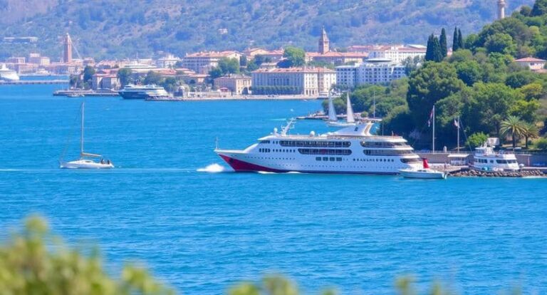 White and red passenger cruise ship near a harbor with a town and green hills in the backgroundpe