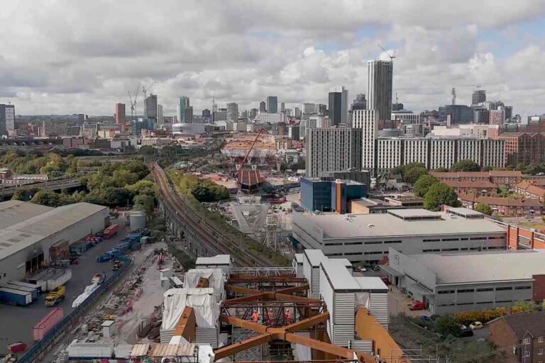 Aerial view of a city skyline with tall buildings and a construction crane in the foreground, plus a railway yard below.