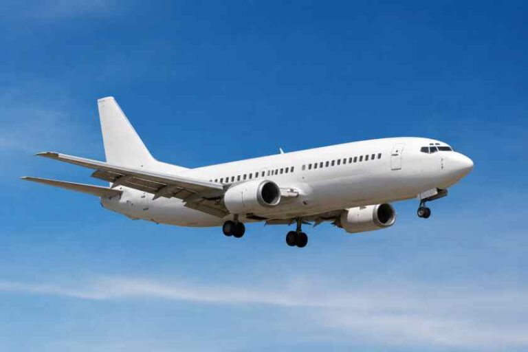 White commercial airliner in level flight against a clear blue sky, landing gear extended.
