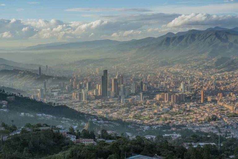City skyline of Medellín nestled in a valley with surrounding mountains and blue sky.