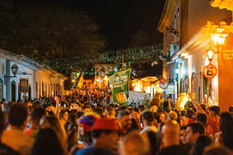 Crowded nighttime street festival with string lights, lanterns, and banners between old buildings.