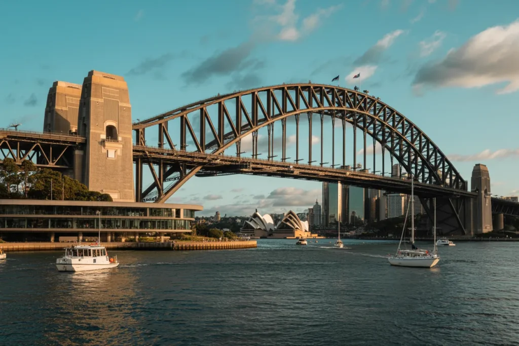 Sydney Harbour Bridge arching over calm water with the Opera House in the background and boats in the foreground.