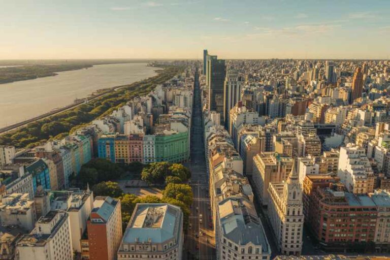 Aerial view of a dense city with a river on the left and a central boulevard lined by tall buildings at sunset