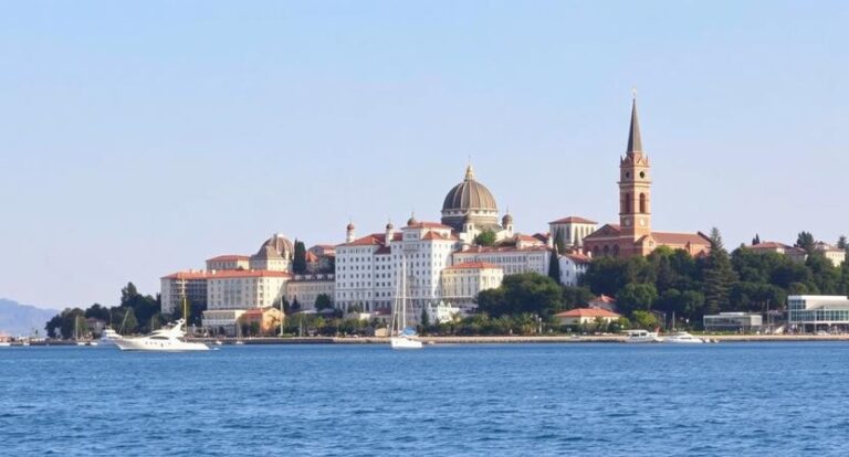 Harbor view of a historic coastal city with a domed building and tall spire on a hill, beside calm blue water.