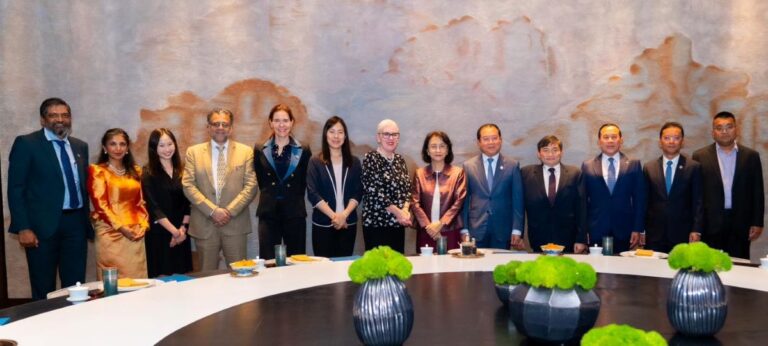 Professional group photo of diverse colleagues in formal attire around a conference table in a boardroom.