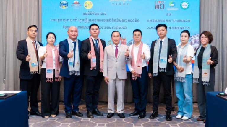 Ten professionals in suits and scarves pose for a group photo at a conference, thumbs up, with a blue event banner in the background.