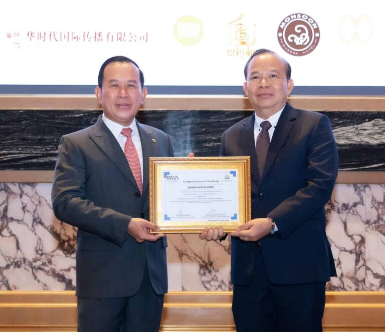 Two men in suits hold a framed certificate at a formal award ceremony on a marble stage backdrop.