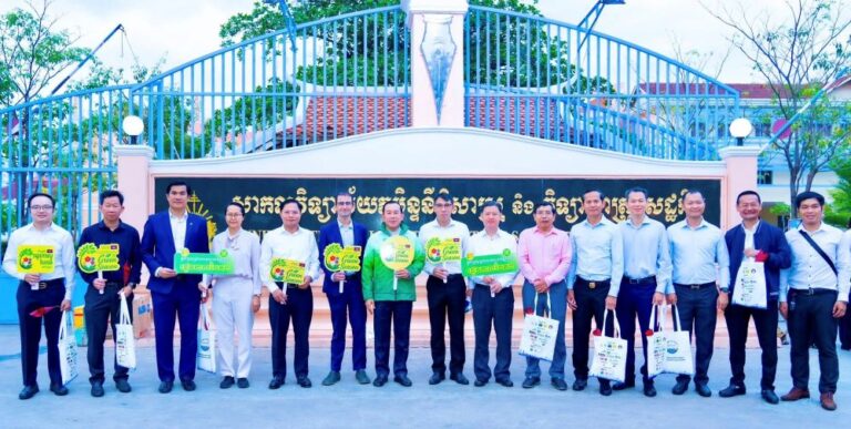 Group of professionals posing for an outdoor group photo in front of a sign, holding green promotional signs and tote bags.