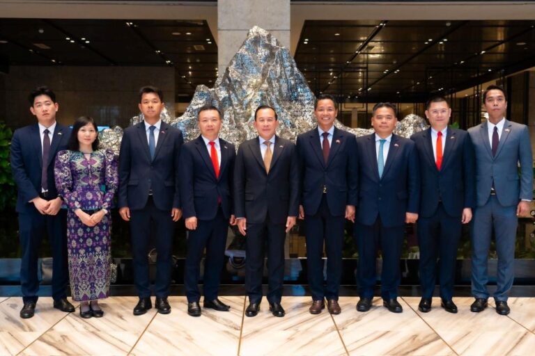 Nine professionally dressed individuals standing side by side in a modern indoor lobby with a metallic mountain sculpture behind them, posing for a group photo.