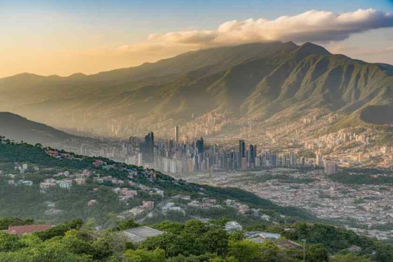 City skyline nestled in a valley with green hills and distant mountains at sunset