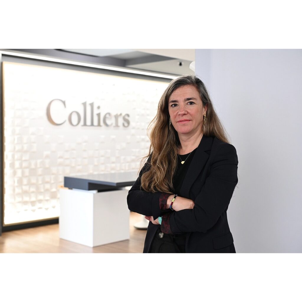 Professional woman in a black blazer standing with arms crossed in a modern office lobby, Colliers sign visible in background.