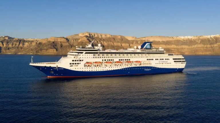 White and blue cruise ship sailing near a rocky cliff coastline under a clear blue sky.