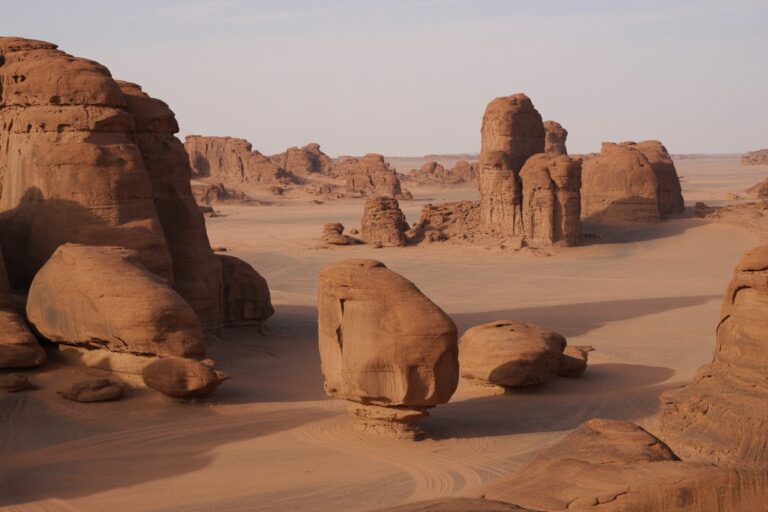 Desert scene with tall sandstone rock formations and smooth sand dunes under a pale sky
