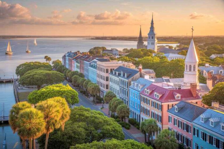 Pastel-colored row houses line a harbor at sunset, with palm trees and church steeples in the background.