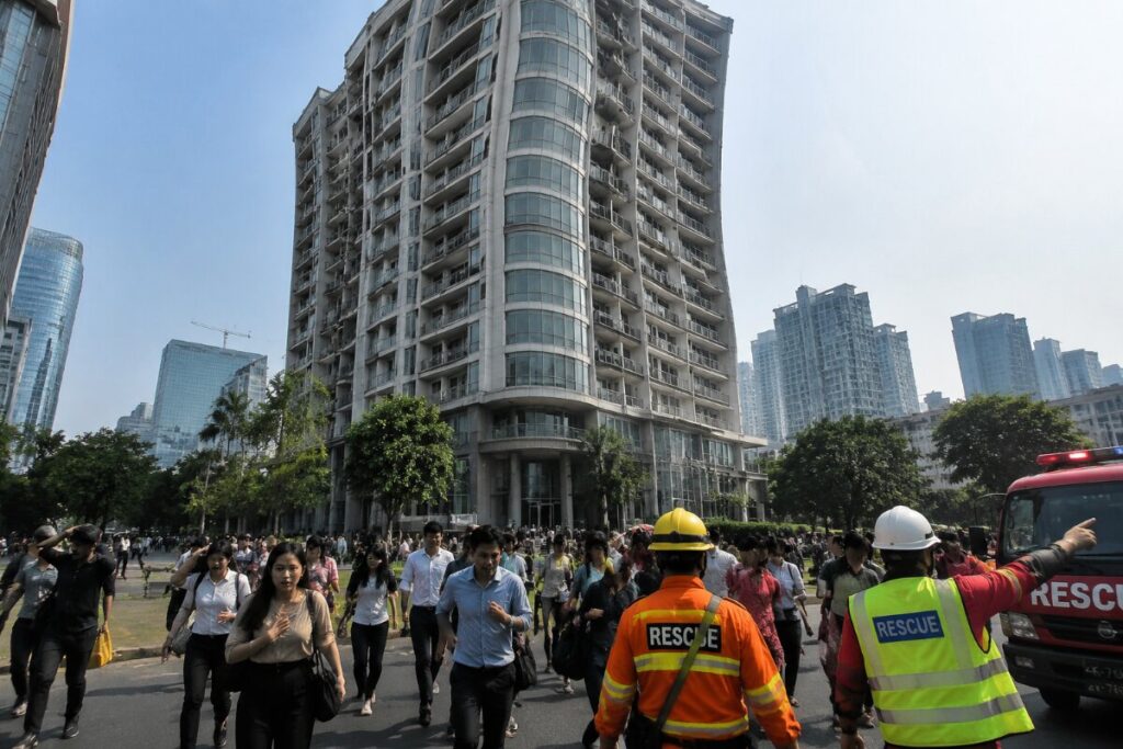 Crowd evacuating a city street past a curved glass high-rise, with rescue workers guiding people in bright vests.